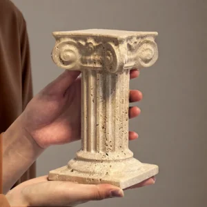 Hands holding a small natural travertine marble Roman column, showcasing its size and porous stone texture