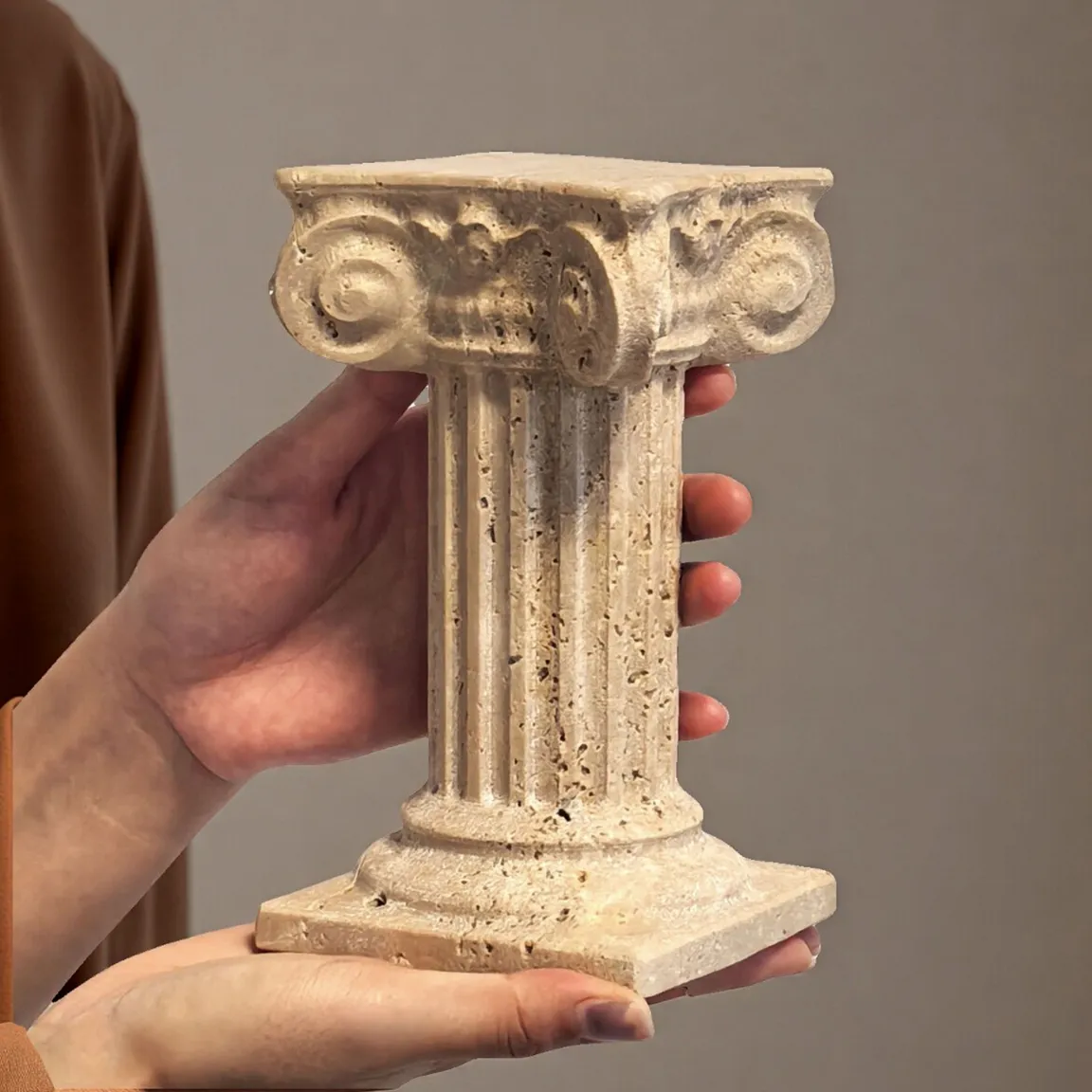 Hands holding a small natural travertine marble Roman column, showcasing its size and porous stone texture
